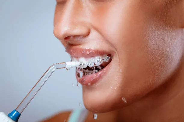 a woman with braces using a water flosser to maintain her oral hygiene