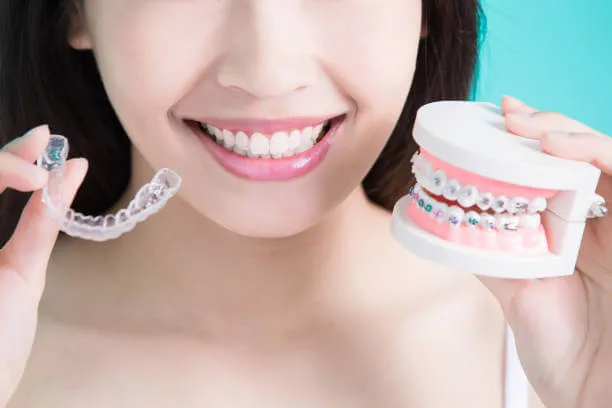 a person holding clear aligners and metal braces on a teeth model